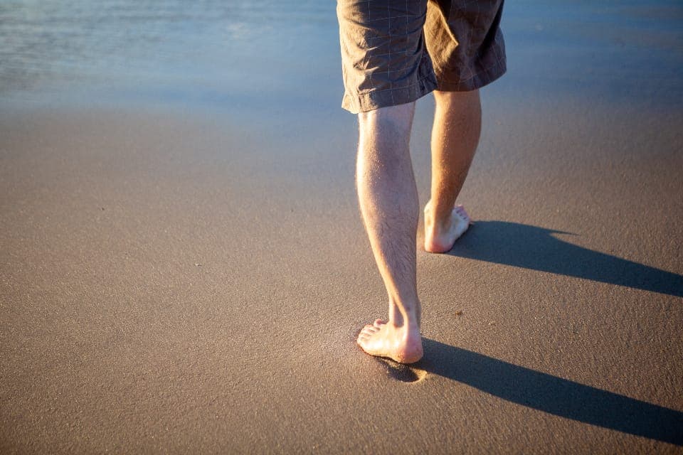 A broad bare foot beside a wide-lasted minimalist running shoe