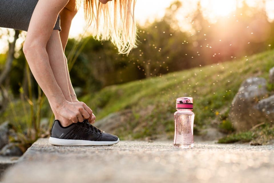 A runner lacing a thin-soled shoe on a path at first light